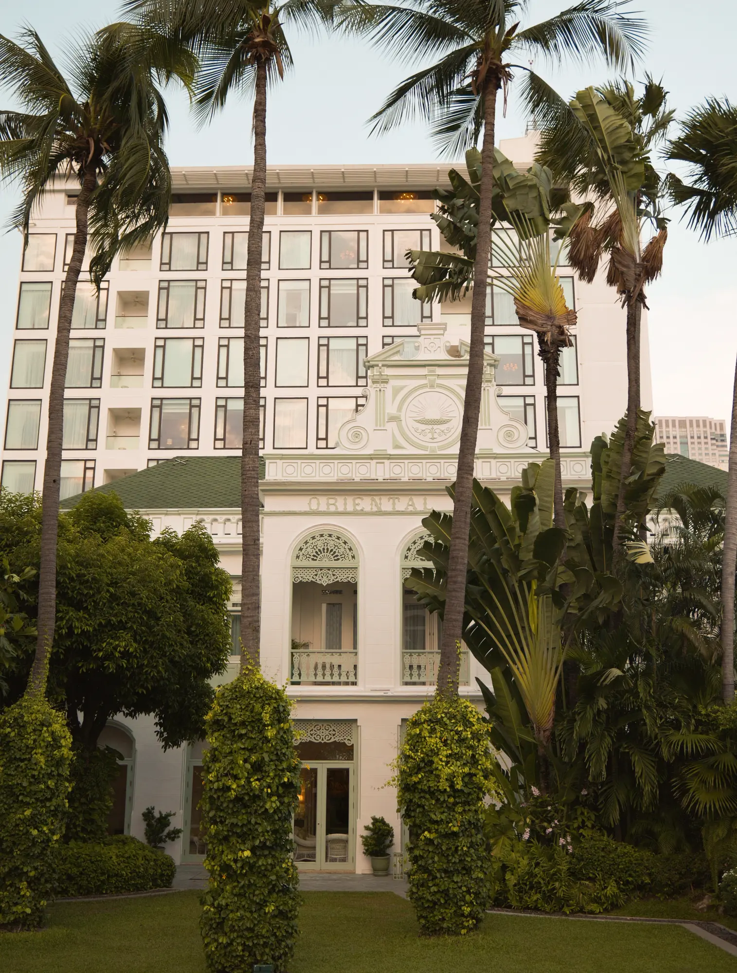 A colonial-era building framed by palm trees and clipped hedges